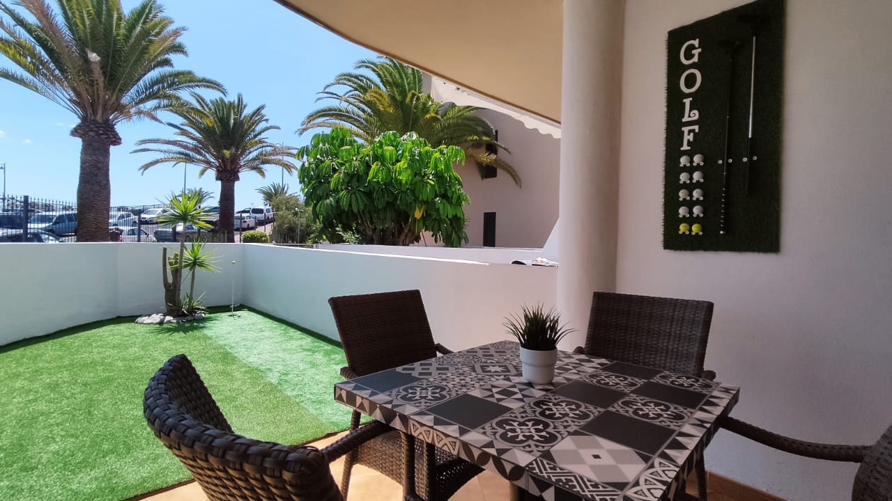 Spacious terrace with outdoor dining area and golf-themed decor, surrounded by palm trees and a view of the garden